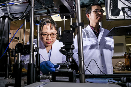 NTU Singapore research associate Liliana Tjahjana (left) loading a sample made of perovskites and gold onto a visible light detector, with Nanyang Assistant Professor Wong Liang Jie, also from the University, monitoring the set-up.